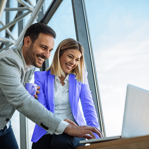 man and woman in an office, leaning over a laptop computer